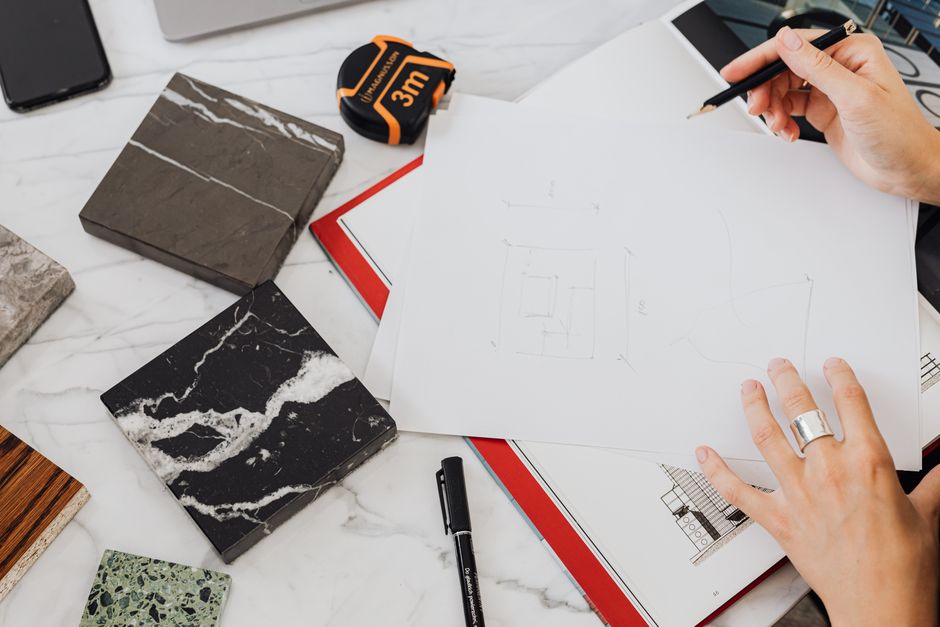 Hands holding architectural sketches with marble samples and measuring tape on a desk.